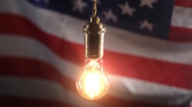 Amerika 'nın bayrak arka planında Edison ampulü yanıp sönüyor. Elektrik fiyatları, faturalar, enerji krizi, vergi artışı. Yüksek kalite 4k görüntü