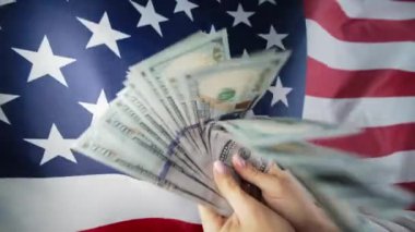 Amerikan bayrağının arka planında sallanan para dolarları. Maliye, ekonomik kriz, Birleşik Devletler para birimi, bağımsızlığın sembolü. Yüksek kalite 4k görüntü