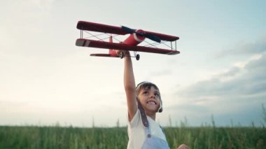 Havacı kasklı mutlu çocuk arka planda yaz sahasında eski model uçak oyuncağıyla koşuyor. Çocukların hayali pilot olmaktır. Git, her yere seyahat et, kaygısız, aktif çocukluk hayatı.