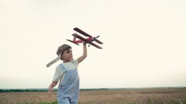 Havacı pilot kasklı mutlu çocuk arka planda şehrin dışındaki çayır alanda eski model uçak oyuncaklarıyla koşuyor. Çocukların hayali pilot olmaktır. Eğlence, yaratıcı hayal, fantezi. Yüksek kalite.