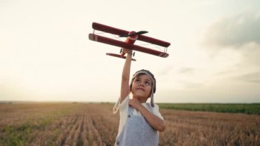 Gülümseyen 5 yaşındaki çocuk tahta uçakla oynuyor, gelecekteki mesleki ilgisini keşfediyor, hayalperest çocuk uçuyor, yaz sahasında seyahat ediyor. Yaratıcı hayal, fantezi, çocukluk. 4k