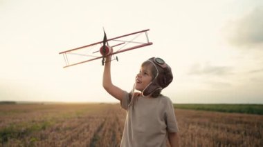 Gülümseyen 5 yaşındaki çocuk tahta uçakla oynuyor, gelecekteki mesleki ilgisini keşfediyor, hayalperest çocuk uçuyor, yaz sahasında seyahat ediyor. Yaratıcı hayal, fantezi, çocukluk. 4k