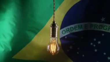 Titrek klasik Edison Tungsten filament lambası sallanan Brezilya bayrağı arka planı. Güney Amerika, Brezilya 'da elektrik tedariği, faturalar, enerji krizi için gümrük vergilerini arttırıyorum. Yüksek kalite 4k