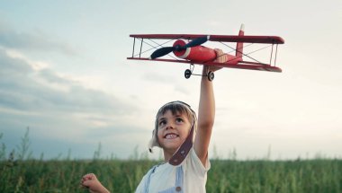 Gülümseyen 5 yaşındaki çocuk tahta uçakla oynuyor, gelecekteki mesleki ilgisini keşfediyor, hayalperest çocuk uçuyor, yaz sahasında seyahat ediyor. Yaratıcı hayal, fantezi, çocukluk. 