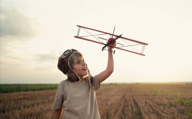 Gülümseyen 5 yaşındaki çocuk tahta uçakla oynuyor, gelecekteki mesleki ilgisini keşfediyor, hayalperest çocuk uçuyor, yaz sahasında seyahat ediyor. Yaratıcı hayal, fantezi, çocukluk.