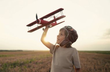 Gülümseyen 5 yaşındaki çocuk tahta uçakla oynuyor, gelecekteki mesleki ilgisini keşfediyor, hayalperest çocuk uçuyor, yaz sahasında seyahat ediyor. Yaratıcı hayal, fantezi, çocukluk.