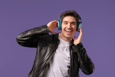 Müzik dinleyen olumlu bir adam, Violet stüdyosunun arka planında modern kulaklıklarla dansın tadını çıkarıyor. Radyo, kablosuz modern ses teknolojisi, çevrimiçi çalar. Yüksek kalite