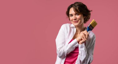 Pembe arka planda fırçası olan genç beyaz kadın sanatçı. Yaratıcı kişi, fantezi, fikir, hayata standart olmayan yaklaşım. Yüksek kalite