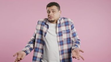 Melez bir adam, omuzları yukarıda. Yardımcı olamıyor, bir jest yapıyor. Bilmiyorum. Zor soru, suçlu tepkisi, pembe arka plandaki kafası karışmış genç adam. Yüksek kalite 4k