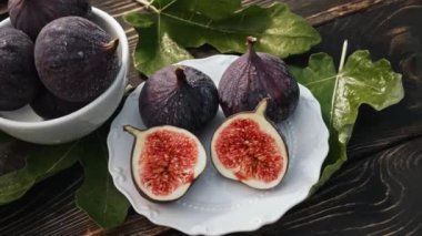 Beyaz tabakta yaprakları olan taze incir, kırsal ahşap masa. Ficus carica. Güzel mevsimlik meyveler, vejetaryen yemekleri. Üst Manzara. Dolly kaydırma atışı. Yüksek kalite 4k görüntü