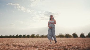 Müstakbel kadın bebek bekliyor. Sağlık hamileliği, mutlu annelik. Uzun elbiseli hamile bir kadın açık alanda tek başına yürüyor, karnını okşuyor. Yüksek kalite 4k görüntü