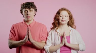 Sakin çift dinleniyor, meditasyon yapıyor. Kadın ve erkek sakinleşir, derin derin nefes alır. Pembe stüdyo arka planında dua eden ellerle. Yüksek kalite 4k görüntü