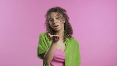 Çekici, Afro-Amerikalı, hipster giymiş genç bir kadın pembe duvar arkasında kameraya hava öpücüğü gönderiyor. Sevimli moda bayan portresi. Yüksek kalite 4k görüntü