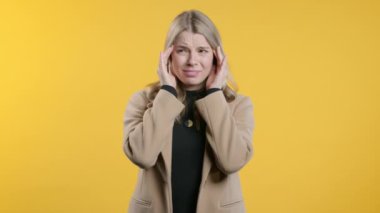 Baş ağrısı, kan basıncı, stüdyo fotoğrafı olan genç bir kadın. Kız ellerini başının üstüne koyuyor, sarı arka planda izole edilmiş. Sorun kavramı, ilaç, hastalık. Yüksek kalite 4k