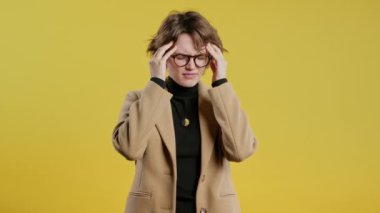 Baş ağrısı, kan basıncı, stüdyo fotoğrafı olan genç bir kadın. Kız ellerini başının üstüne koyuyor, sarı arka planda izole edilmiş. Sorun kavramı, ilaç, hastalık. Yüksek kalite 4k