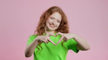 Gülümseyen kadın kalbinin şeklini gösteriyor. Pembe üzerine pozitif kadın. Sevgi. Kadın sağlığı, gönüllülük, bağış, minnettarlık sembolü, flört konsepti. Yüksek kalite 4k görüntü