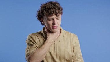 Yakışıklı kıvırcık adamın yarası var. Mavi stüdyoda boğazı şişmiş bir adam var. Anjin ağrısı. Genç adam acı hissediyor. Mevsimsel grip, soğuk algınlığı. Yüksek kalite 4k görüntü