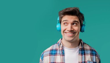 Müzik dinleyen olumlu bir adam, mavi stüdyo arka planında modern kulaklıklarla dansın tadını çıkarıyor. Radyo, kablosuz modern ses teknolojisi, çevrimiçi çalar. Yüksek kalite