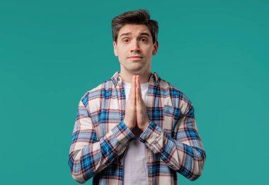 Genç adam mavi arka planda parmaklarıyla dua ediyor. Adam birine arzularını tatmin etmesi için yalvarıyor, yardım ediyor, sınavda şans için dua ediyor. Yüksek kalite 