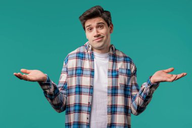 Kafası karışmış adam omuzlarını kaldırır, yardım edemez, bilmediğimi gösterir. Zor soru, suçlu tepkisi, şaşkın stil adamı mavi arka planda.