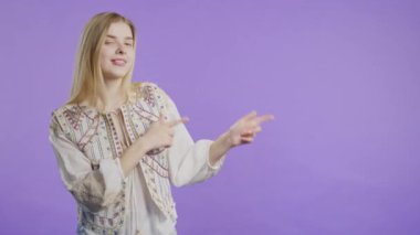 Gülümseyen 20 'li yaşlarda bir bayan reklamınız için boş bir yer arıyor. Önerilen kadın sağ tarafı işaret ediyor, boşluğu kopyalayın. Kadın, menekşe arkaplanda izole bir şey sunuyor. Yüksek kalite 4k