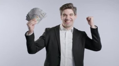 Nakit parası olan mutlu bir iş adamı. Gri duvardaki Amerikan doları banknotları. İkramiyenin, kazancın, zaferin, piyangoyu kazanmanın sembolü. Yüksek kalite 4k görüntü