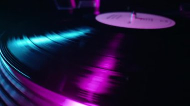 Vinil çalara renkli ışık tutarak dönen bir plak. Yakın çekim görüntüsü. Neon altında canlı bir film. Analog ses ekipmanı konsepti, klasik parti. Yüksek kalite 4k görüntü