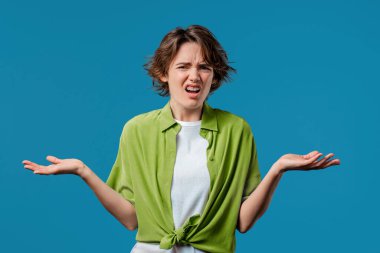 Sinirli bir kadın kamerayı işaret ediyor ve nasıl bir jest yaptığını gösteriyor. Deli misin diye soruyorum. Kavgacı kadın mavi arka planda izole edilmiş. Öfkeli ifade, birini suçlamak..