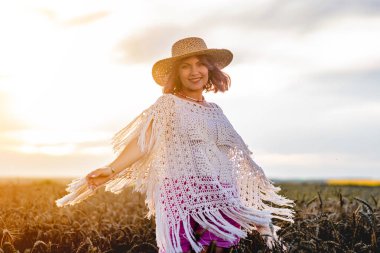  Hasır şapkalı, buğday tarlasında yürüyen boho rustik kadın. Altın saat, ilham. Şaşırtıcı doğa manzarası, kadınsı, boyalı pembe saç stili portresi olan genç bayan. Yüksek kalite