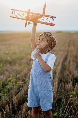 Gülümseyen 5 yaşındaki anaokulu çocuğu tahta eski model uçak oyuncaklarıyla oynuyor, gelecekteki mesleki ilgilerini keşfediyor, hayalperest çocuk uçuyor, seyahat ediyor..