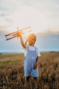 Gülümseyen 5 yaşındaki anaokulu çocuğu tahta eski model uçak oyuncaklarıyla oynuyor, gelecekteki mesleki ilgilerini keşfediyor, hayalperest çocuk uçuyor, seyahat ediyor..