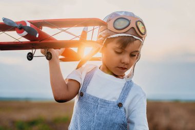 Şehir dışında, doğa çayırında uçağı olan havacı pilot kasklı mutlu çocuk. Çocukların hayali pilot olmaktır. Git, her yere git, kaygısız, aktif çocukluk yaşam tarzı. Yüksek kalite 