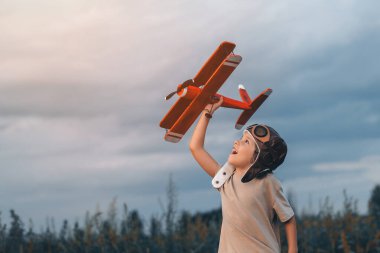 Şehir dışında, doğa çayırında uçağı olan havacı pilot kasklı mutlu çocuk. Çocukların hayali pilot olmaktır. Git, her yere git, kaygısız, aktif çocukluk yaşam tarzı. Uzayı kopyala Yüksek kalite 