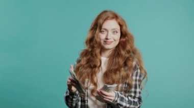 Zengin, heyecanlı, kızıl saçlı, nakit parası olan bir kadın. Mavi duvarda Amerikan doları banknotları. İkramiyenin sembolü, kazanç, zafer, kazanan piyango. Yüksek kalite 4k