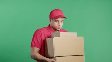 Posta kuryesi ağır bir paket kutusu taşıyor. Postacı yeşil stüdyo geçmişiyle ilgili adres paketini teslim ediyor. Zor iş. Yüksek kalite 4k