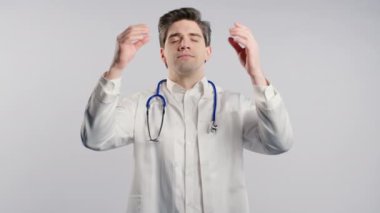 Sakinleşen, meditasyon yapan, stresi reddeden bir doktor. Esmer, yakışıklı hastane çalışanı derin derin nefes alıyor, gri stüdyo geçmişini sakinleştiriyor. Yoga, ahlaki denge, zen konsepti. Yüksek kalite 4k 