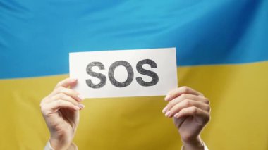 Ukrayna ulusal bayrağında SOS, alarm ve acil durum kartı olan kadın eller. Ukrayna işçi sömürüsü, savaş, işgal, insan kaynakları, yardım talebi, çevre bakımı. Yüksek kalite 4k