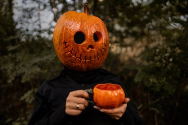 Cadılar Bayramı için balkabağı kafalı, turuncu bardaktan çay ya da kahve içen pozitif gülümseyen bir kadın. Balkabağı kostümü. Şeker mi şaka mı? Yüksek kalite fotoğraf