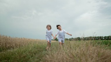Küçük çocuklar buğday tarlasında neşeyle koşuyorlar. Eski moda kıyafetler içinde çocuklar bir arada. Mutlu kardeşler, özgürlük, çocukluk. Yüksek kalite