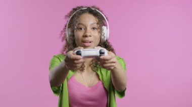 Pembe stüdyo arka planında izole edilmiş joystick ile TV 'de video oyunu oynayan güzel genç bir kadın. Modern teknolojiyi kullanarak. E-spor, hobi, akış