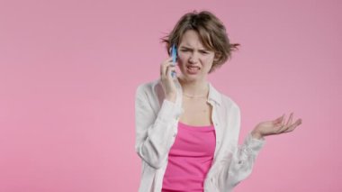 Sinirli genç bir kadın cep telefonuyla konuşurken kavga ediyor. Stresli kızgın bir kadın. Pembe stüdyo geçmişi. Çatışma, anlaşmazlık, olumsuz. Yüksek kalite 4k görüntü