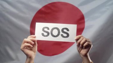 Kadın eli Sos, Alarm, Japon bayrak arkaplanındaki acil durum kartı. Japonya, işgücü sömürüsü, göçmenler, mülteciler, insan kaynakları, yardım talebi, çevre bakımı. Yüksek kalite 4k görüntü