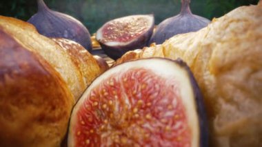 Kamera, dilimlenmiş sağlıklı sulu incir ve kruvasan parçaları arasında dönüyor. Dolly Slider ekstrem makro. Mevsimlik meyve ayrıntıları, Ficus carica. Harika bir kahvaltı. Yüksek kalite 4k görüntü