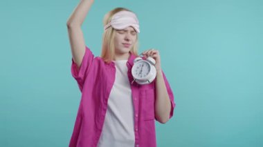 Alarmlı saatle uyandı. Elinde tutan uykulu genç bir kadın. Mavi arka plan. Sabahın 7 'sinde. Tembel kadın yeterince uyuyamadı, zaman geçirme kavramı. Yüksek kalite 4k görüntü