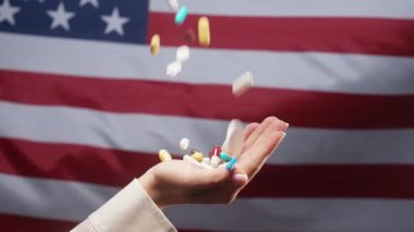 Kadın eli bayrağın üstüne düşen haplar. Amerika Birleşik Devletleri 'nde pahalı ilaçlar. Eczacılık işi. Eczane temalı. Çok renkli ilaçlar ve kapsüller. Yüksek kalite 4k görüntü