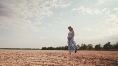 Müstakbel kadın bebek bekliyor. Sağlık hamileliği, mutlu annelik. Uzun elbiseli hamile bir kadın açık alanda tek başına yürüyor, karnını okşuyor. - Evet. Yüksek kalite 4k görüntü