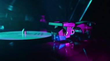 Vinil çalara renkli ışık tutarak dönen bir plak. Yakın çekim görüntüsü. Neon altında canlı bir film. Analog ses ekipmanı konsepti, klasik parti. Yüksek kalite 4k görüntü