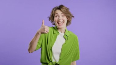 El işaretli şık bir kadın, baş parmak işareti gibi. Mutlu bayan, doğru seçim, harika bir anlaşma, menekşe arkaplan. Pozitif kadın model kameraya gülümser, onay, güven konsepti. kalite