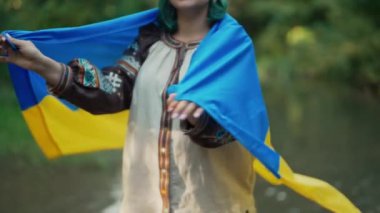 Yeşil Orman Arkaplanında Ulusal Bayrağı Olan Mutlu Gülümseyen Ukraynalı Kadın. İşlemeli Vyshyvanka 'daki gururlu Vatansever Kadın. Özgür Ukrayna. Yüksek kalite 4k görüntü 