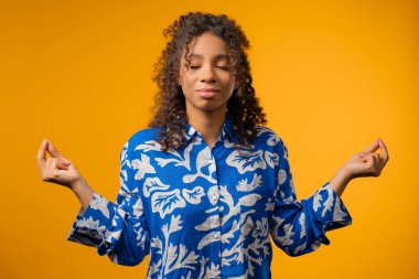 Calm african american woman relaxing, meditating, refuses stress. Curly teenager girl breathes deeply, calms down yellow studio background. Yoga, moral balance, zen concept. High quality clipart